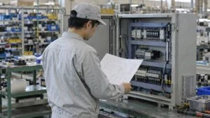 図面と制御盤の配線を見比べる品質保証担当者の後ろ姿