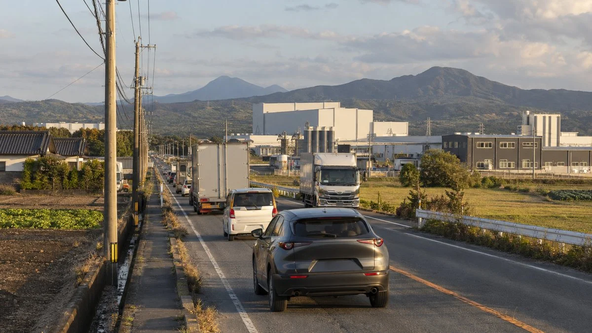工場が建ち並ぶ郊外の幹線道路を走る車とトラック