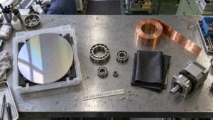 作業台に並ぶシリコンウエハー・ベアリング・銅箔・炭素繊維・減速機