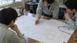机に広げた配管計装図を囲んで確認する技術者